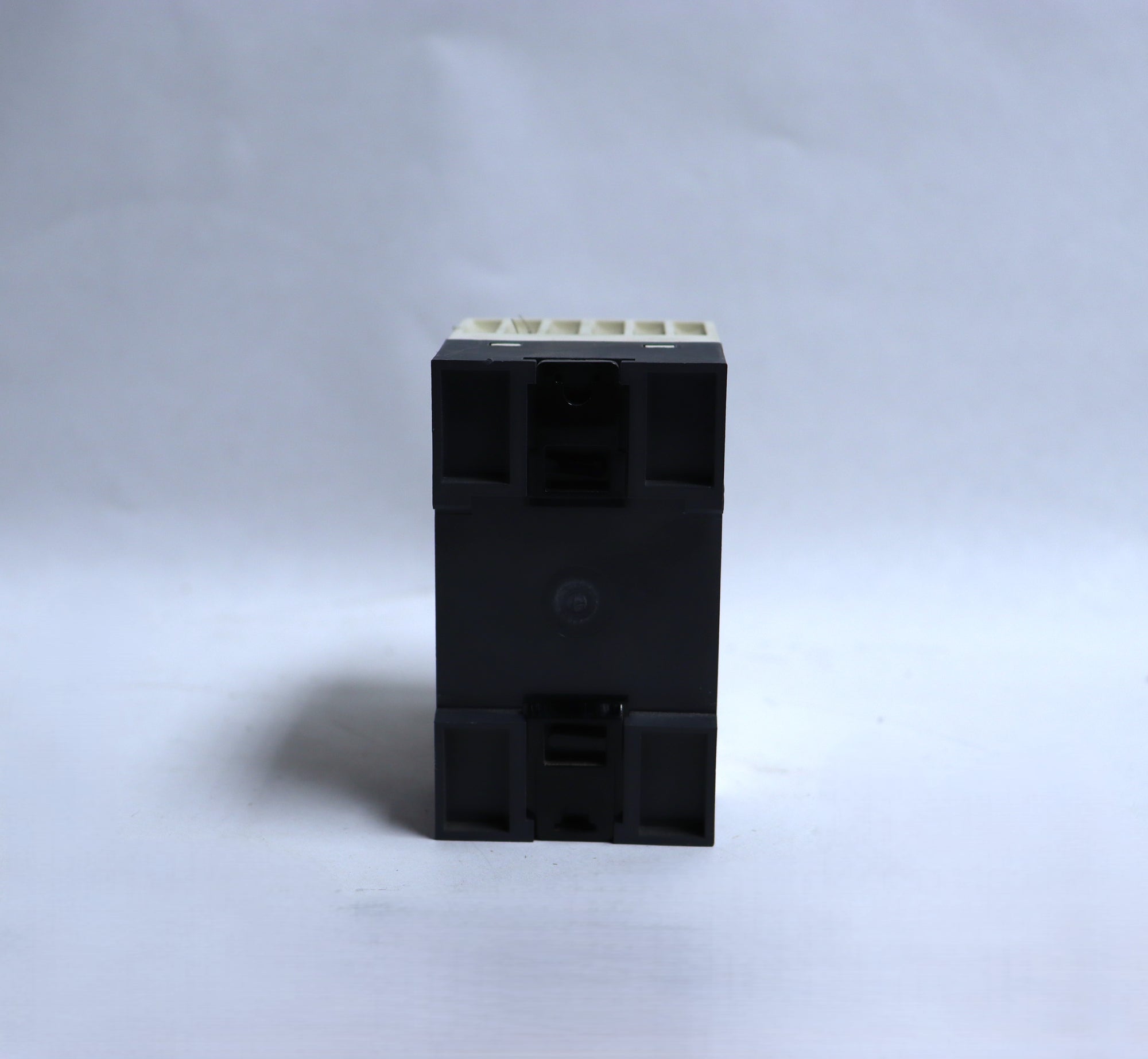 A small black plastic electrical component or terminal block with a light beige connector strip on top, photographed upright against a plain light gray background.